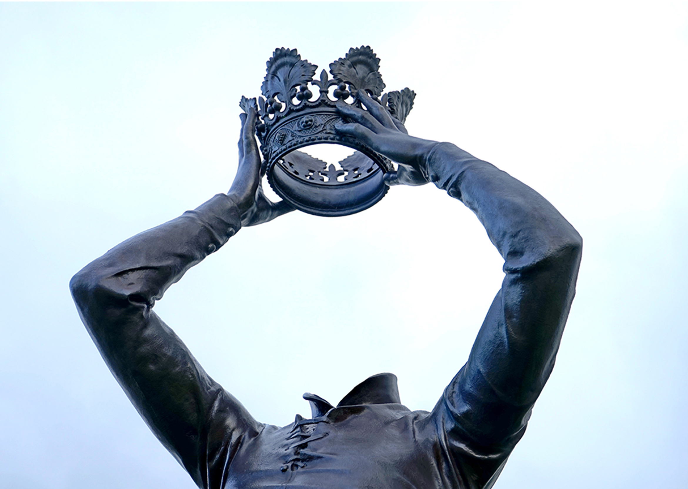 A headless statue holds a crown in the sky