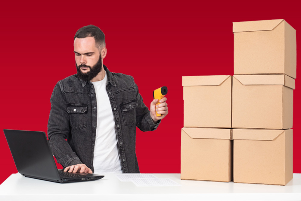 A man points a barcode reader at a stack of boxes while checking his computer.