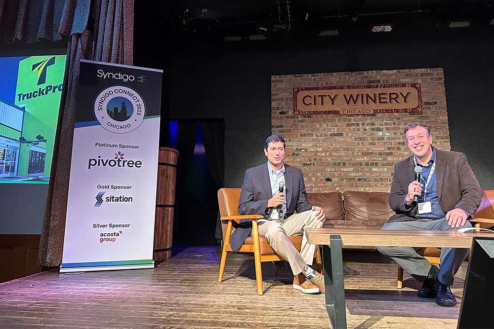 2 men on stage having a fireside chat at a conference.